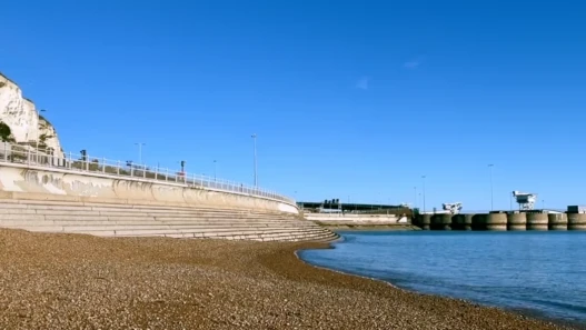 A still showing the eastern port and shingle beach at Dover, with the white cliffs to the left and the ferry port to the right
