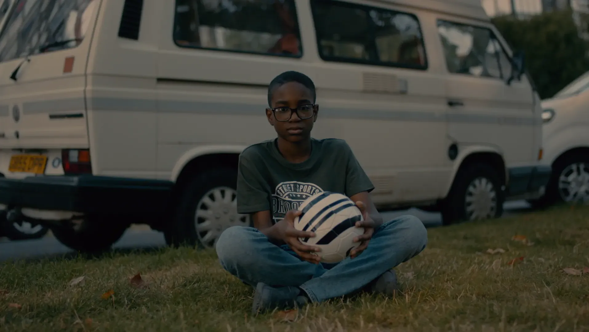 A young black boy sitting on the grass crossed legged with a football in his hand