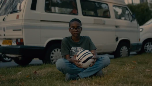 A young black boy sitting on the grass crossed legged with a football in his hand