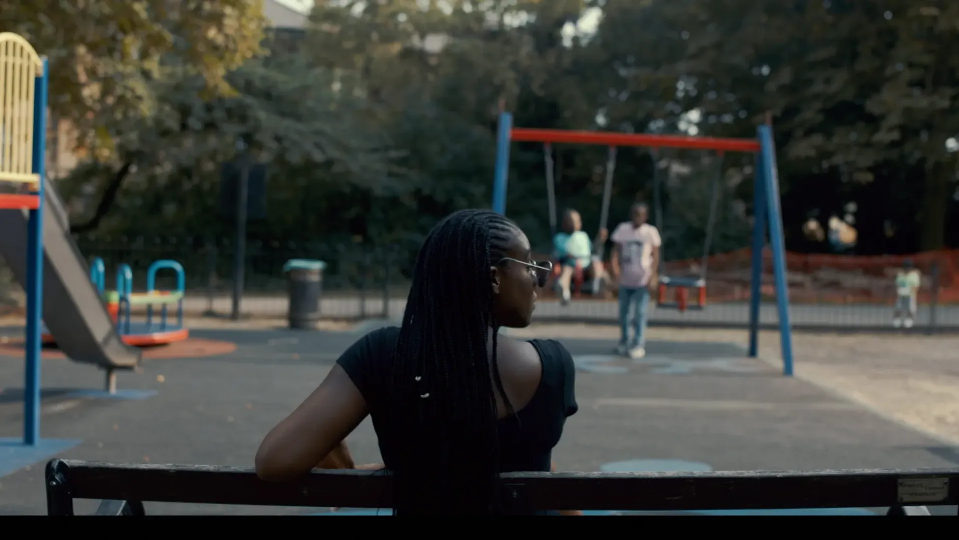 A mother seated at the park watching her kids play.