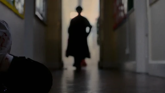 A dark figure in black approaches a wounded school student on the floor