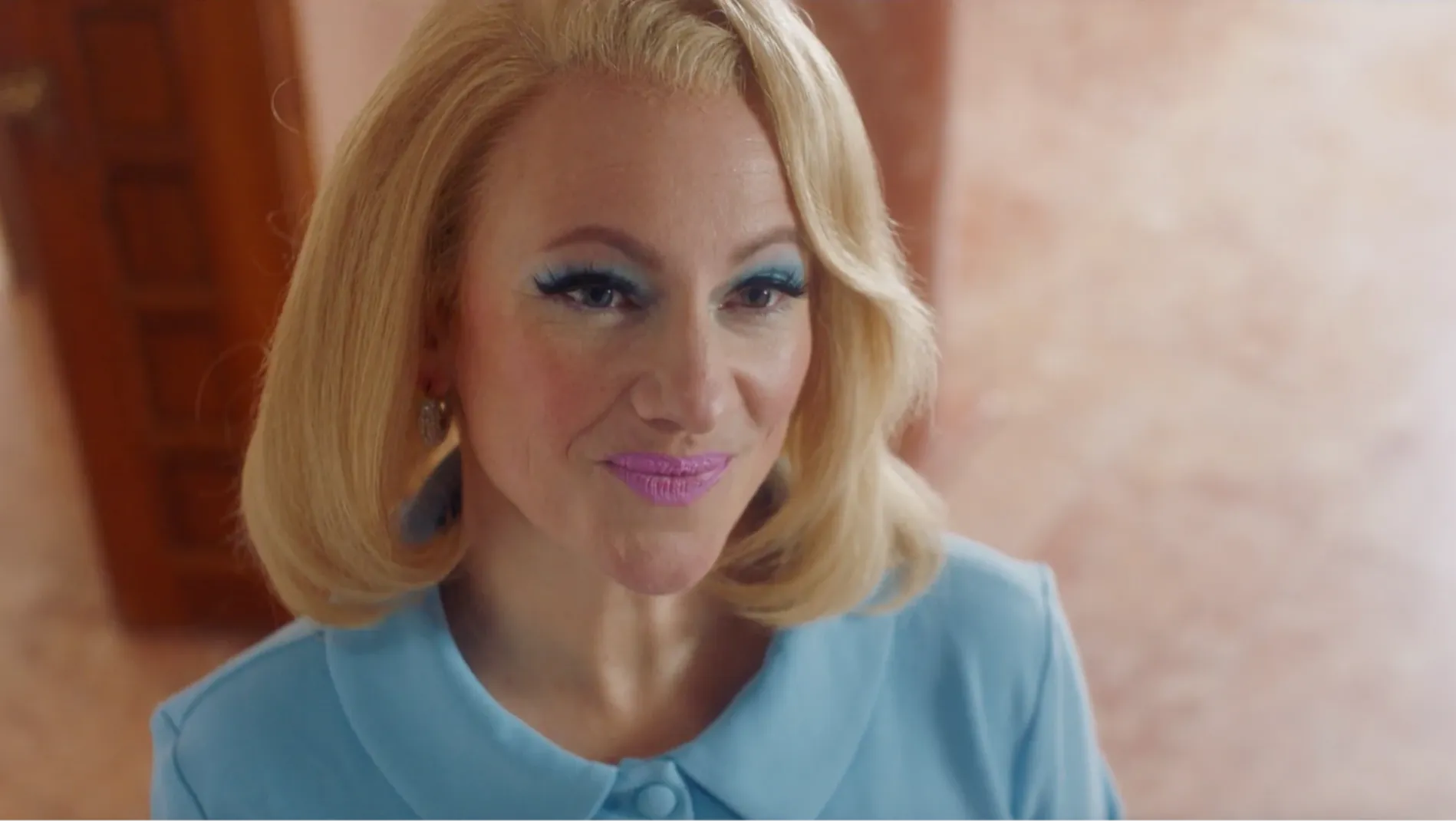 This image shows a woman dressed in a blue suit with bold makeup.