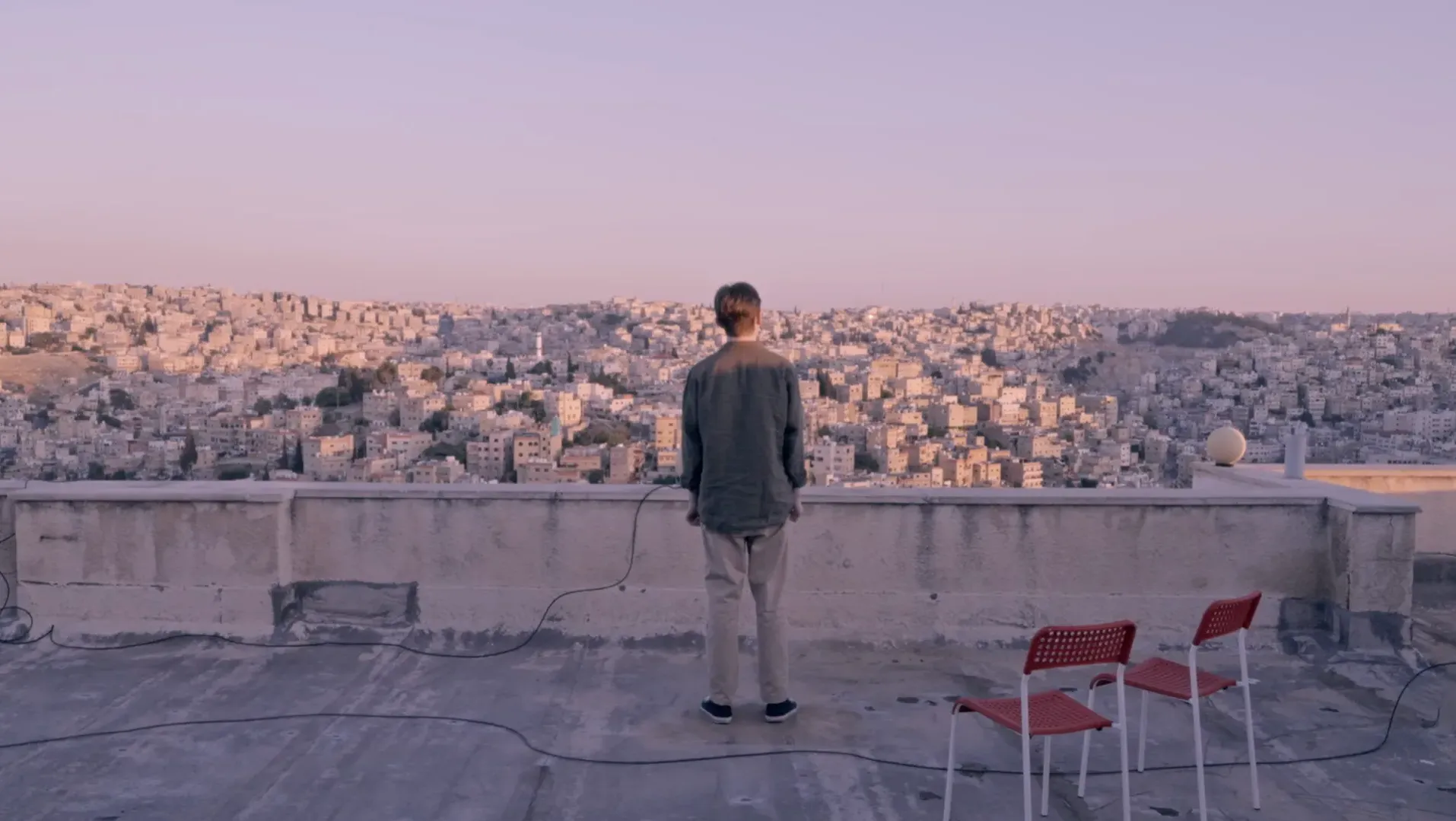 Man standing on a rooftop overlooking a Middle Eastern city at sunset