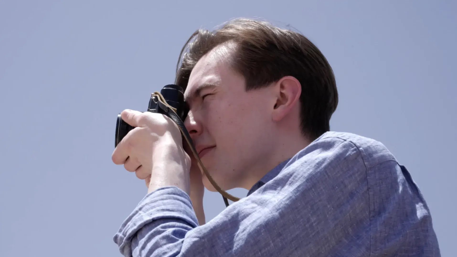 Close up of a young man holding a camera against a blue sky
