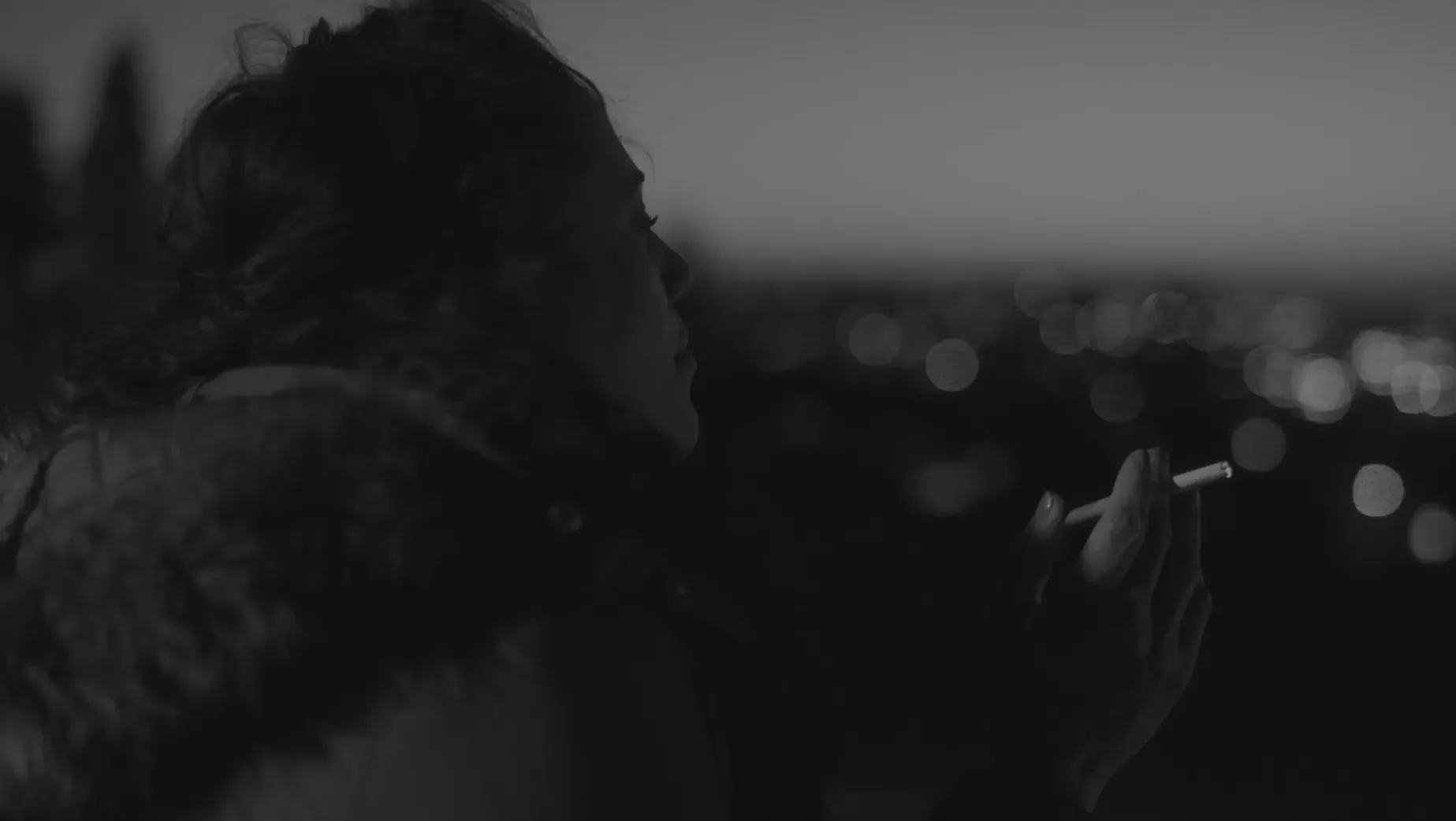 A black and white side-view close up of a woman holding a cigarette in a moment of pause