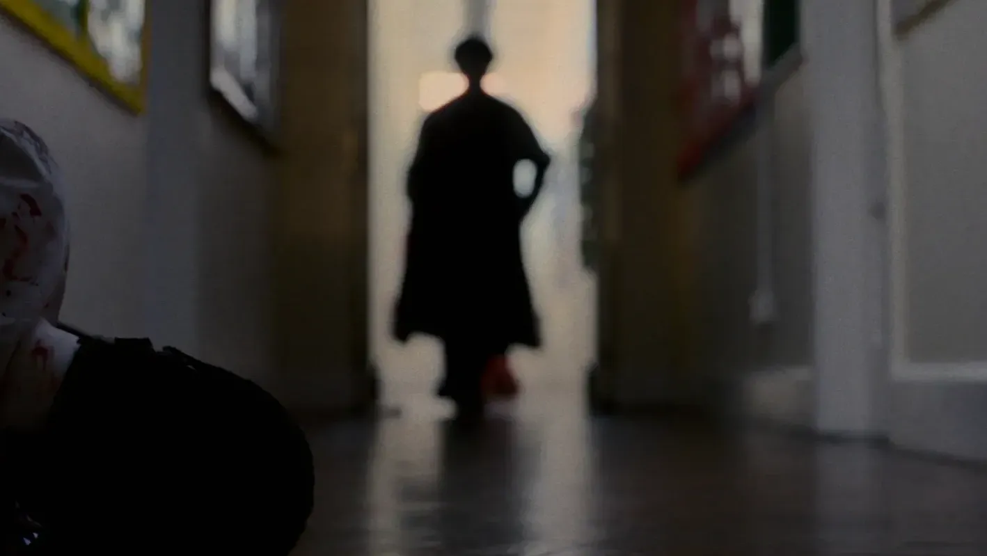 A dark figure in black approaches a wounded school student on the floor