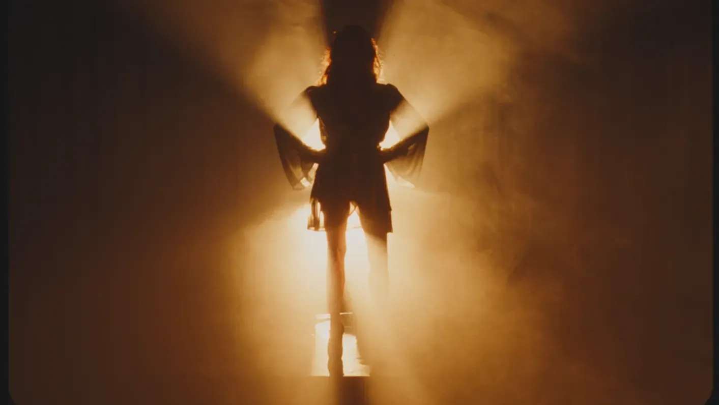 A woman’s silhouette pauses before her long-awaited entrance to an adoring crowd.