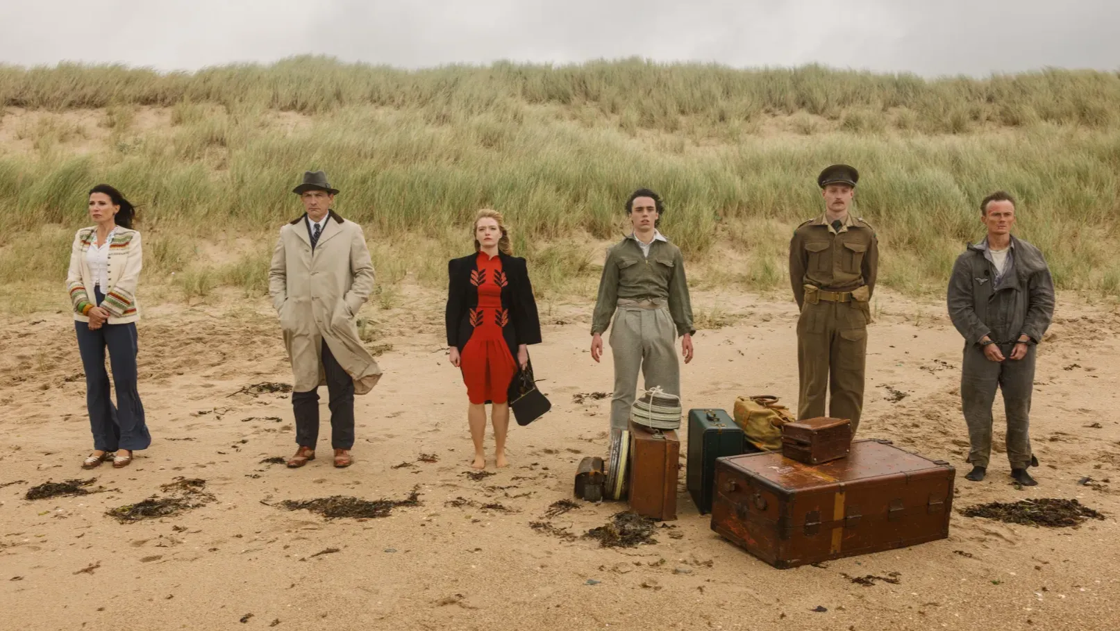 Six figures stand on a windy beach.