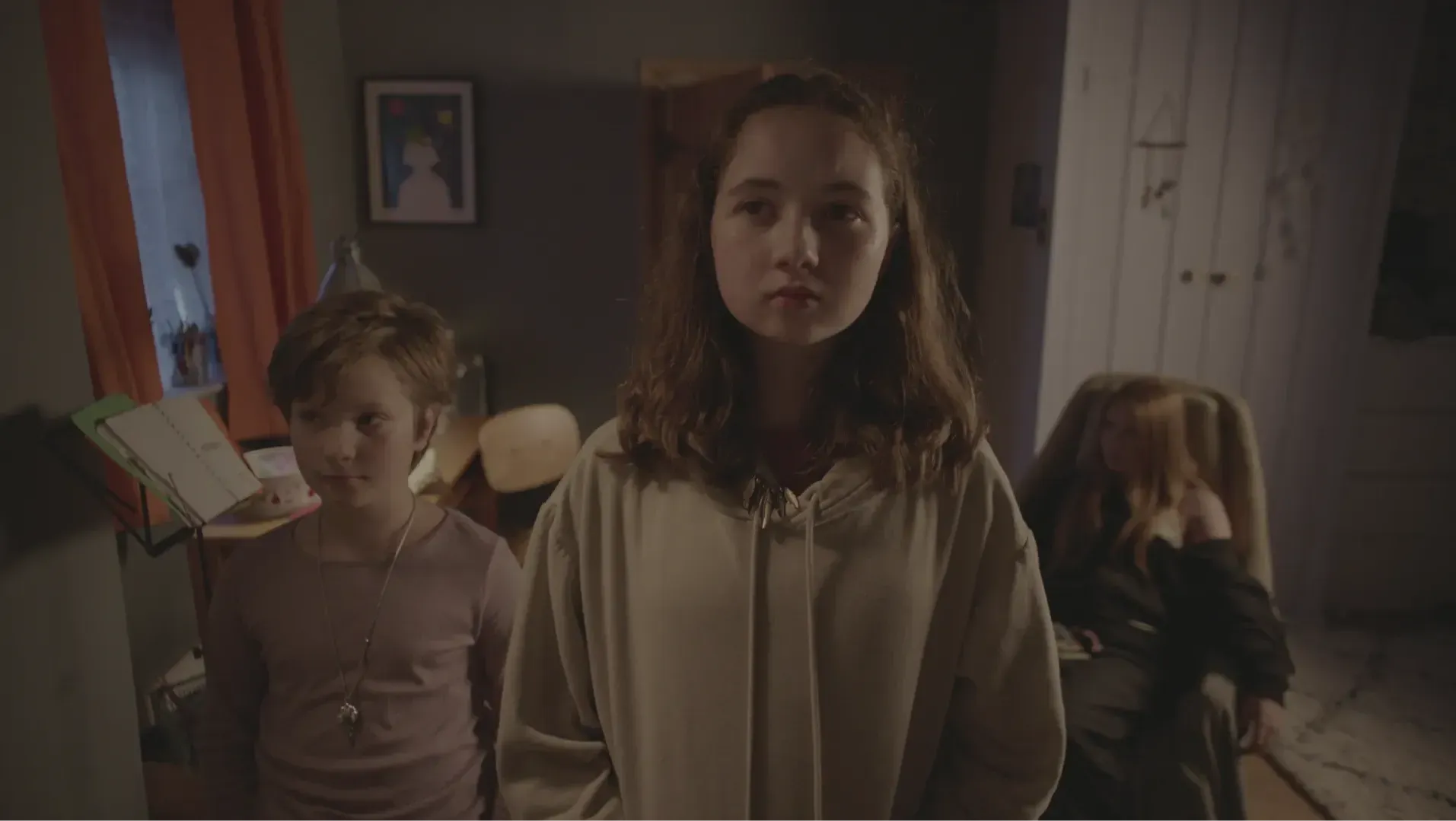 Two children stand and one child seated inside a room.