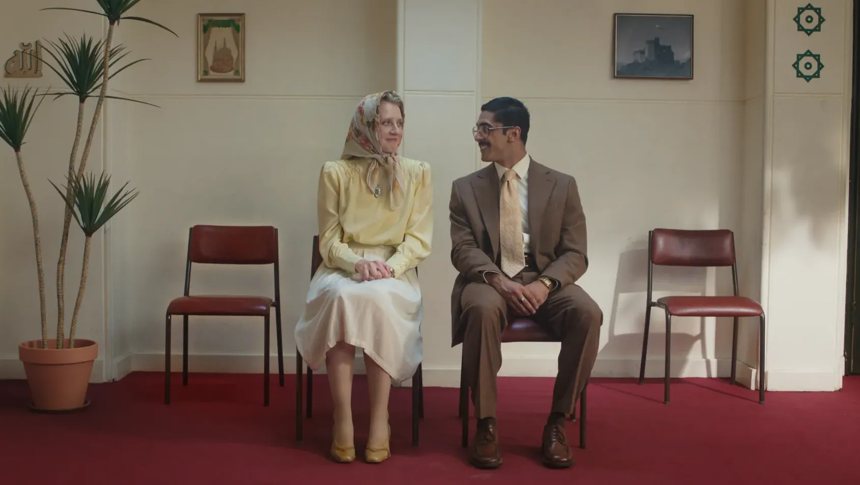 A smartly dressed woman and man sit side by side in the waiting  room, sharing a quiet smile.