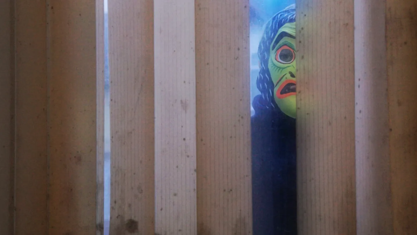 Boy in a mask peeking through dirty blinds and widow