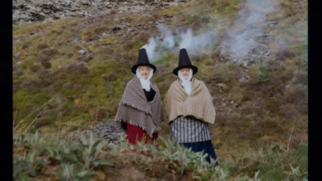 Two women dressed in traditional Welsh clothing, wearing stove pipe hats.