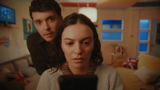 A woman is looking at a phone while a man leans over her shoulder watching her in the mirror