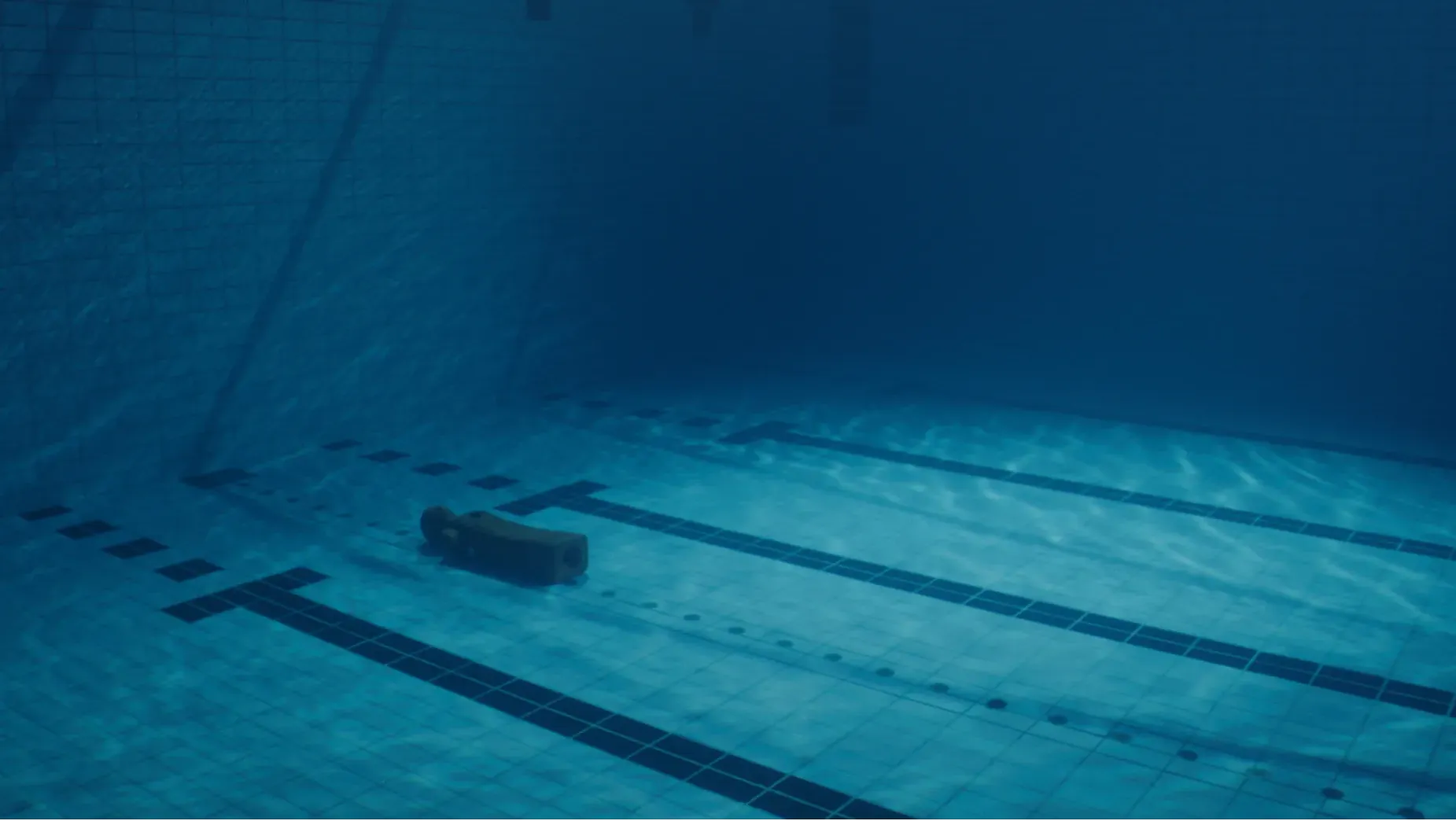 A rescue dummy underwater, laying on the bottom of a swimming pool.