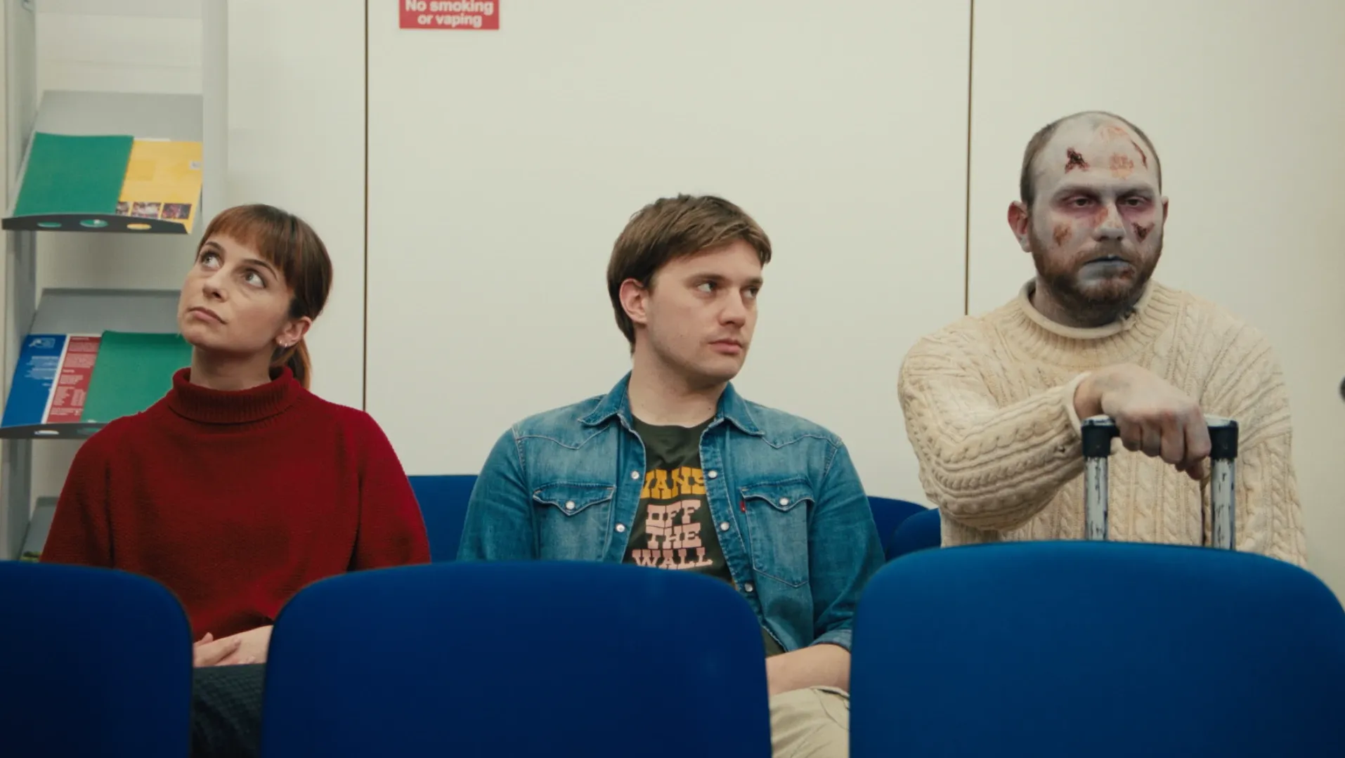 A couple and a zombie sit in a waiting room