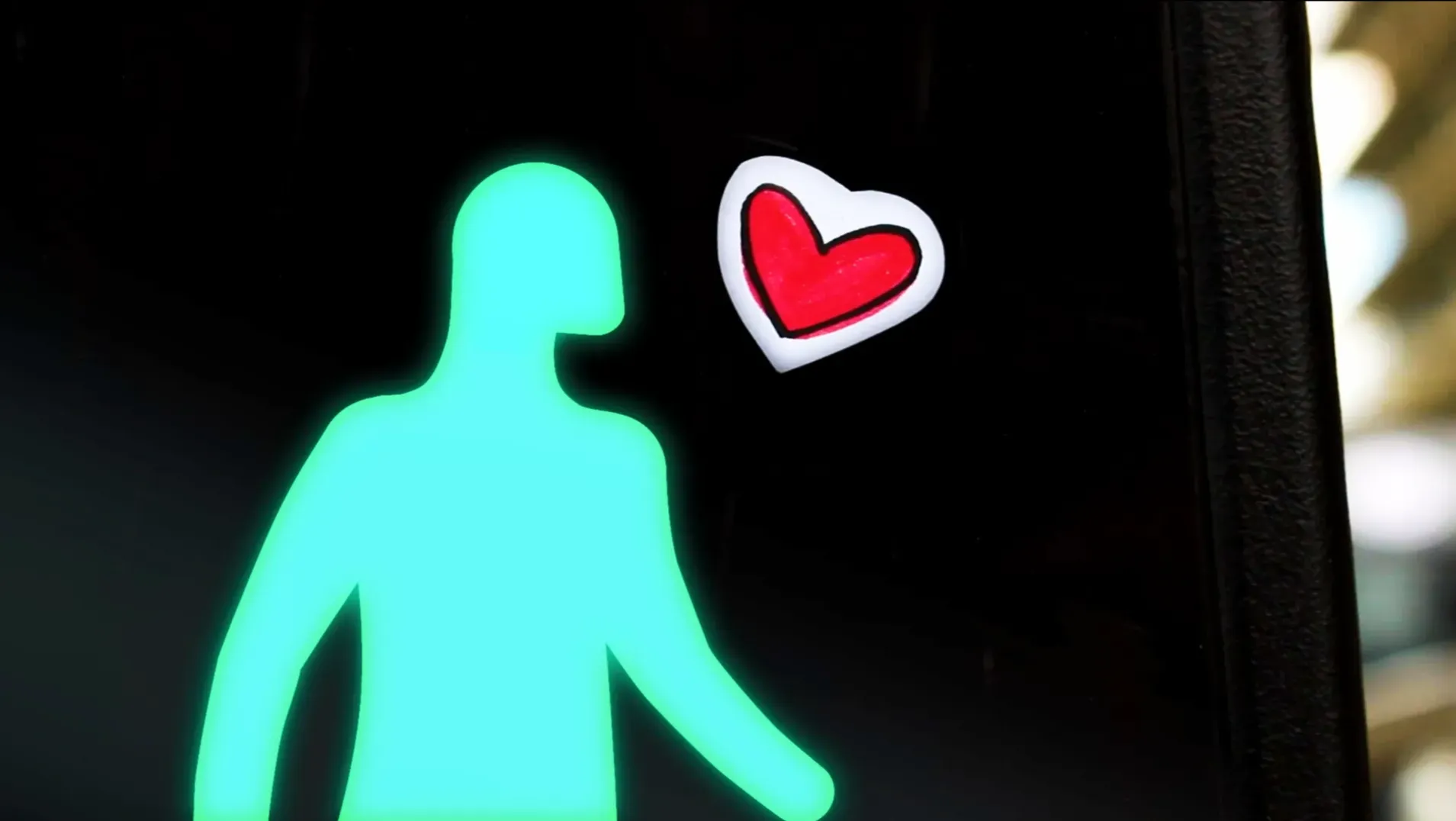 A traffic light green man stands next to a sticker of a cartoon heart