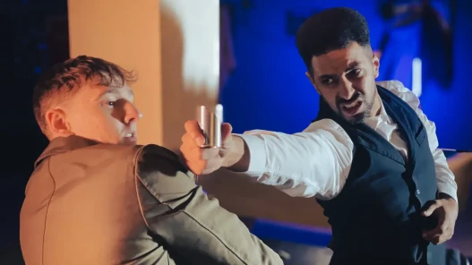 A man holds a shot glass and tries to hit another man with it but the other man dodges out of the way and looks at the shot glass