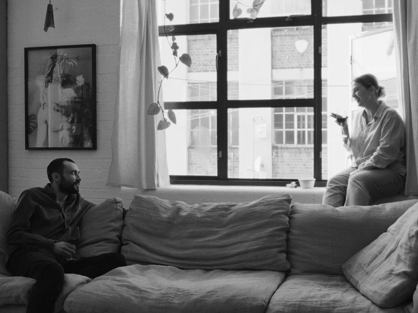 A black and white image of two people talking in a living room.