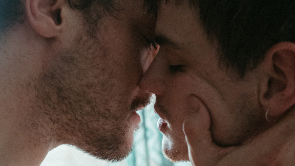 Two men embrace, one holds the other's face in his hand.