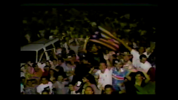 Still from JUNIOR TU PAPÁ (2024) of football fans celebrating in the street.