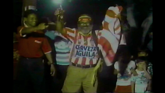 Still from JUNIOR TU PAPÁ (2024) of football fans celebrating in the street.