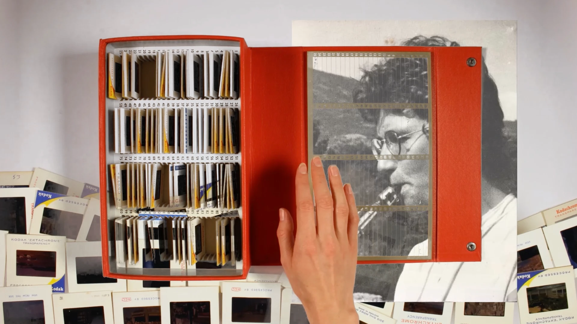 A hand over box of photograph slides. Behind the box is a man playing the clarinet.