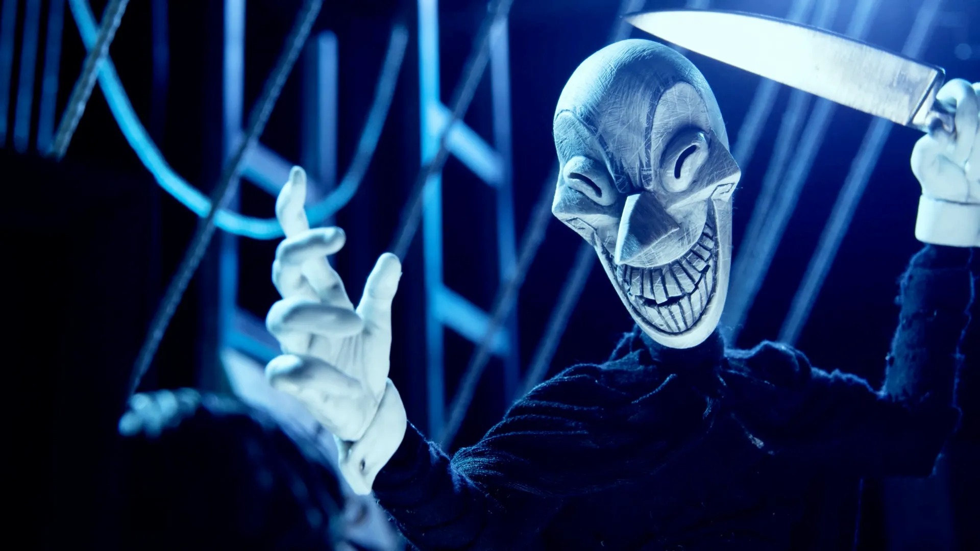A menacing masked figure in a cloak holds up a knife with a scary smile