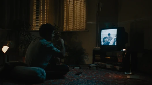 A man drinking tea watching old family VHS tapes on a TV.