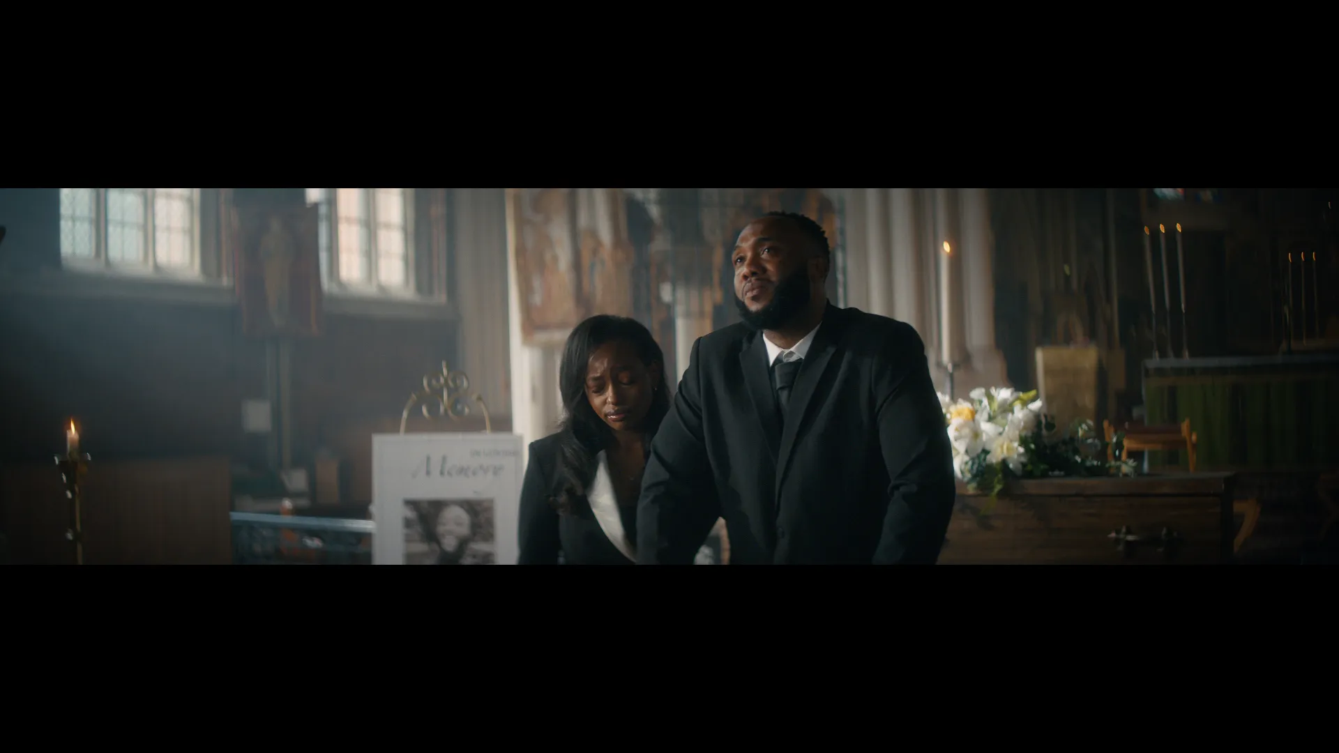 Two people standing in front of a coffin, in a church