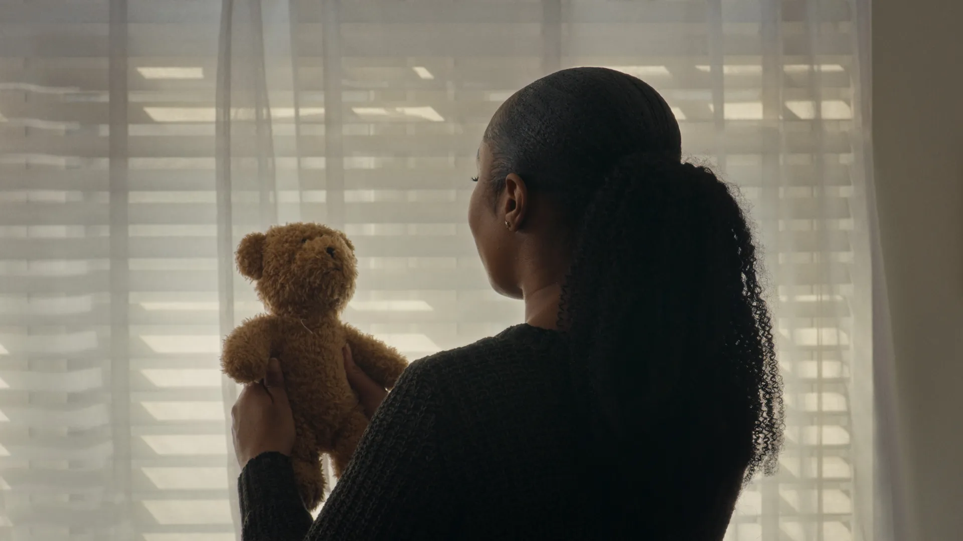 Woman holding a teddy standing in front of a window