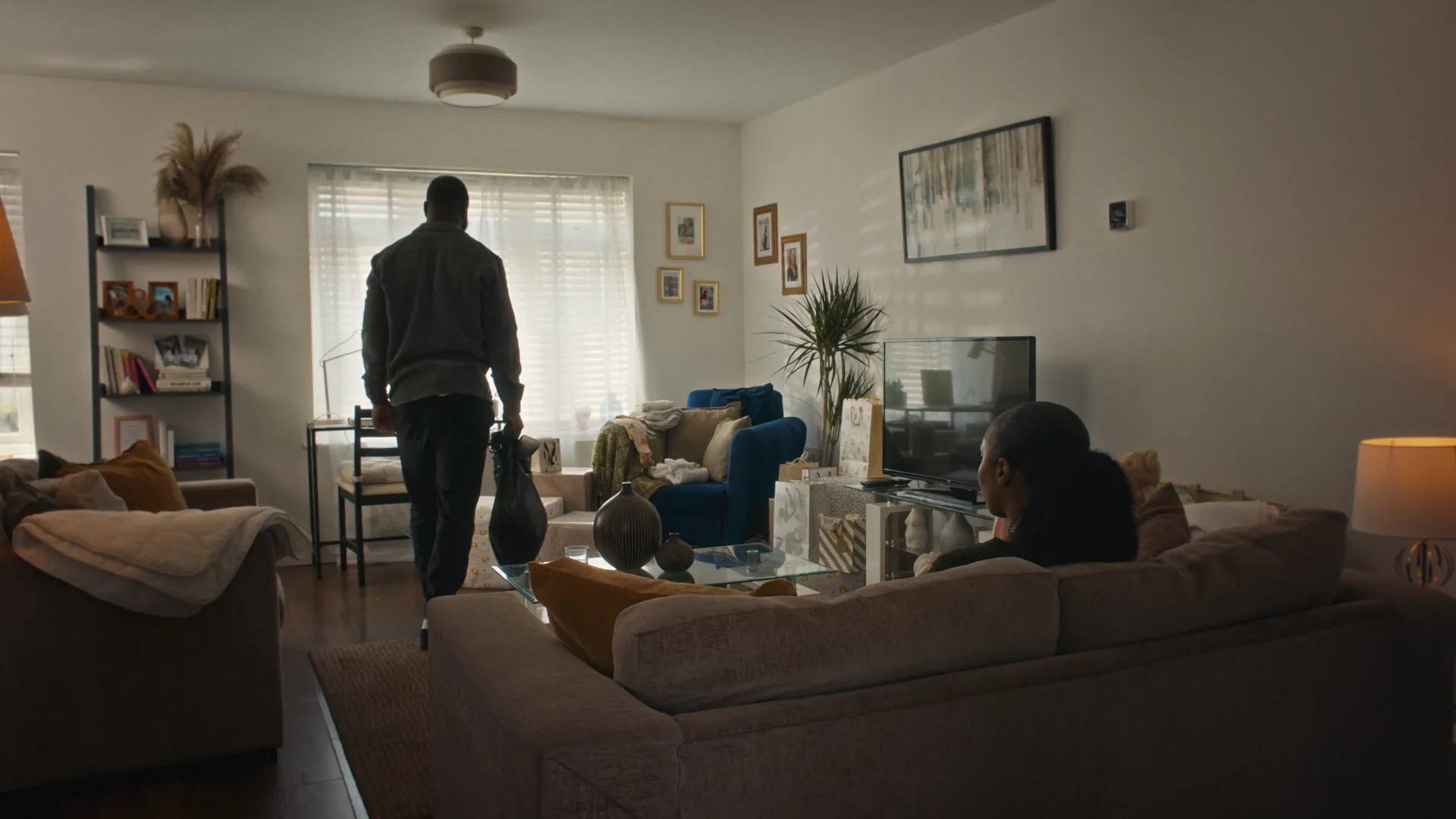 Man holding black bag, woman sat on sofa, in living room