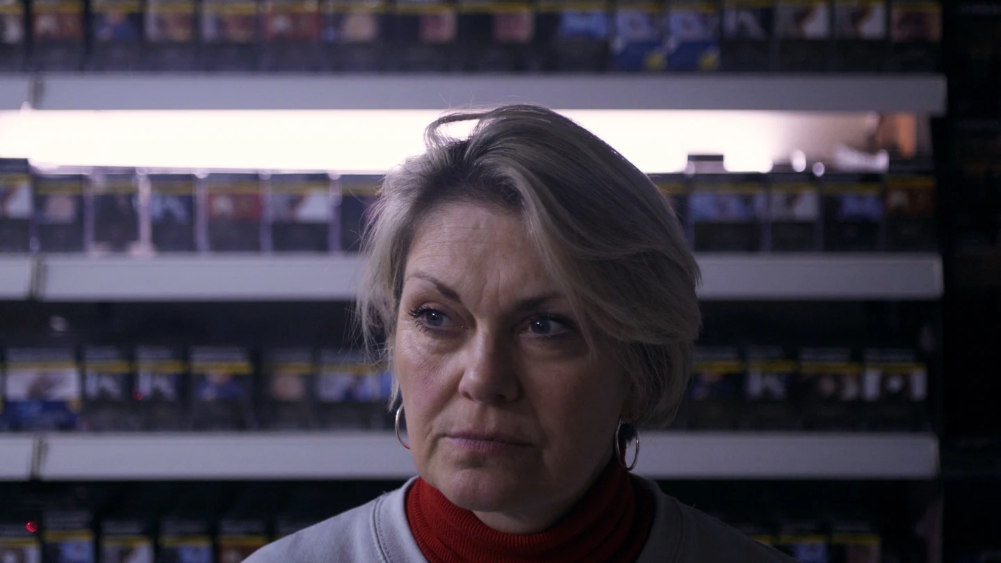 Woman in a convenience store gazing into distance with cigarette packets in the background