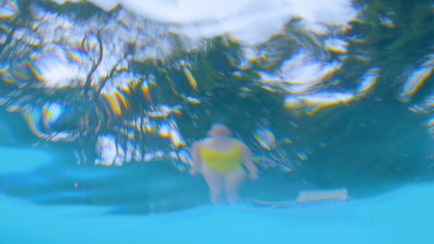 distorted view through water of a woman in a yellow bathing costume at the edge of a swimming pool