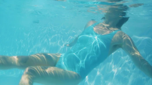 Girl in blue bathing suit in a swimming pool floating underwater