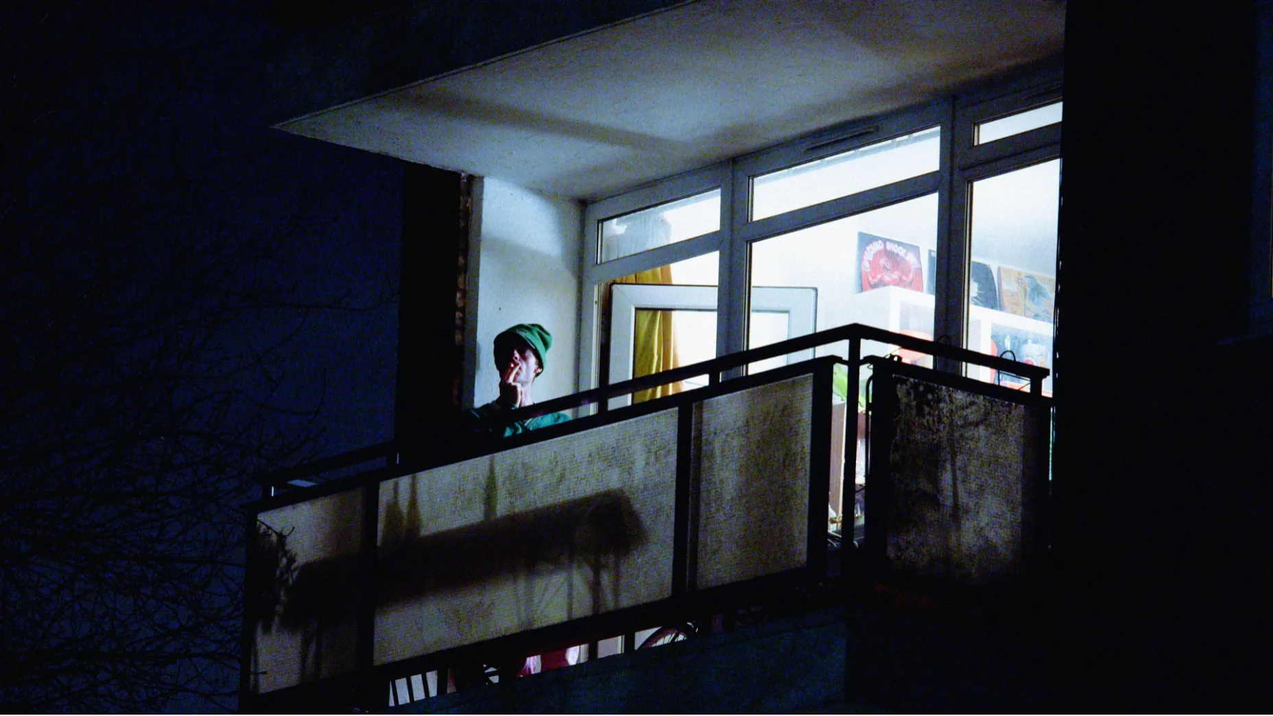 A man is seated on his balcony smoking a cigarette