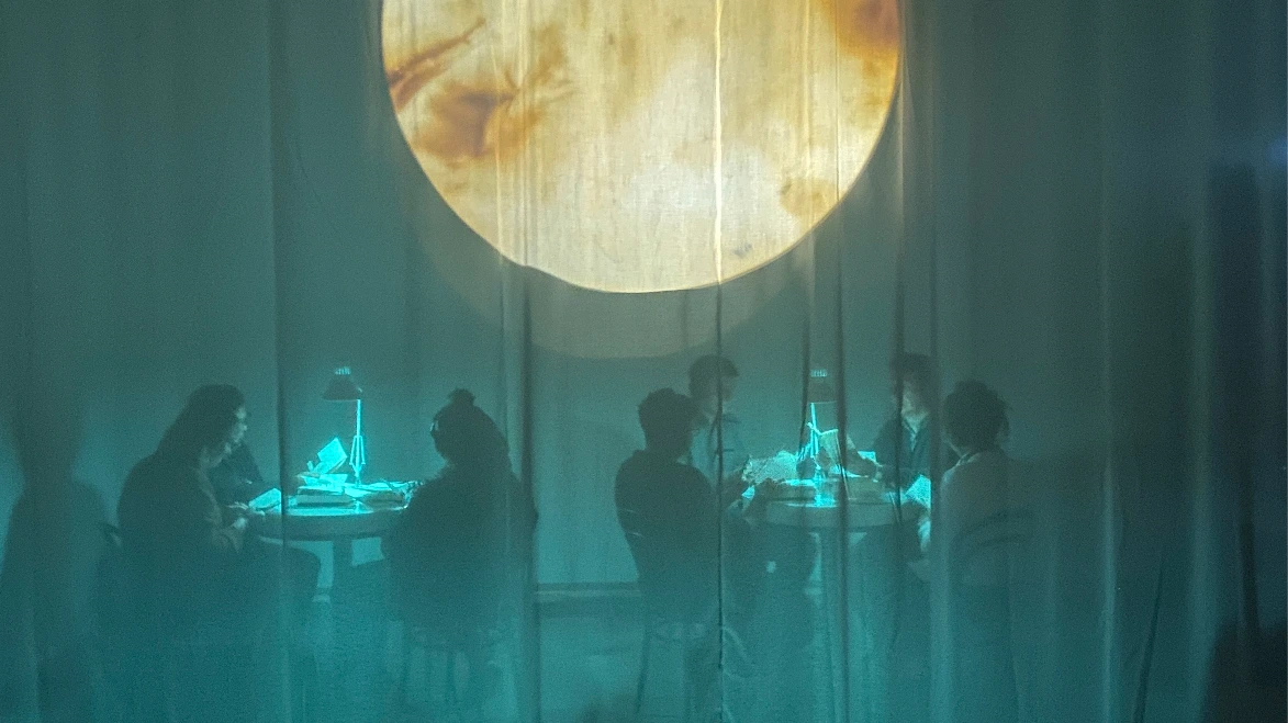 The sillouettes of people through a gauze curtain, reading books in a green light.