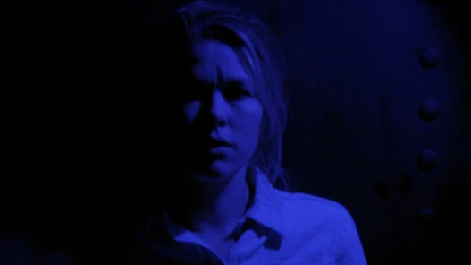 A woman in a dark room looks frightened at something off camera