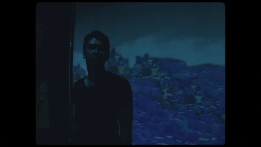 A young man looks excitedly at something off camera in a dark room