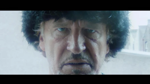 A man wearing a Russian hat looks directly into the camera