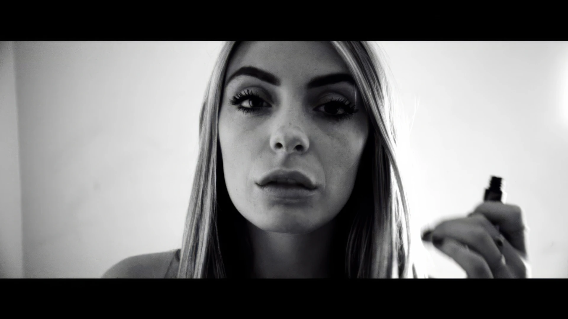 A young woman putting on makeup shows her face to the camera
