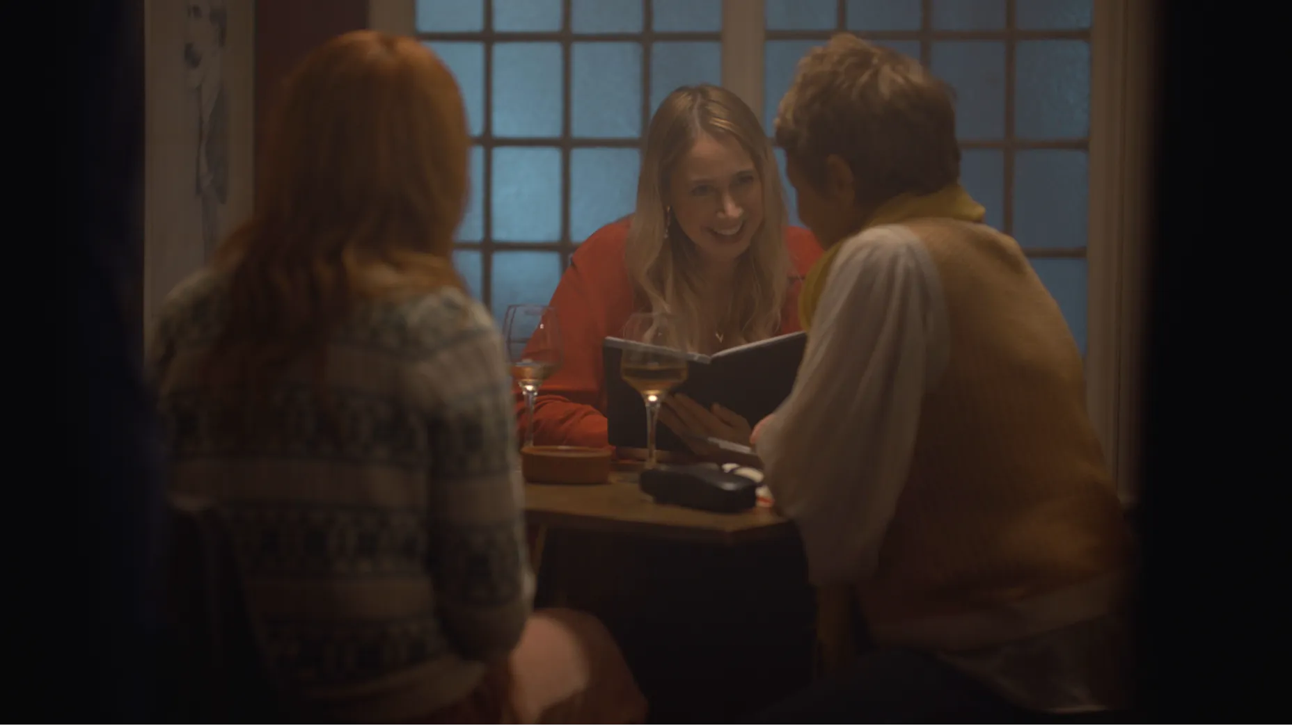 Three women sit at a pub table reading a book