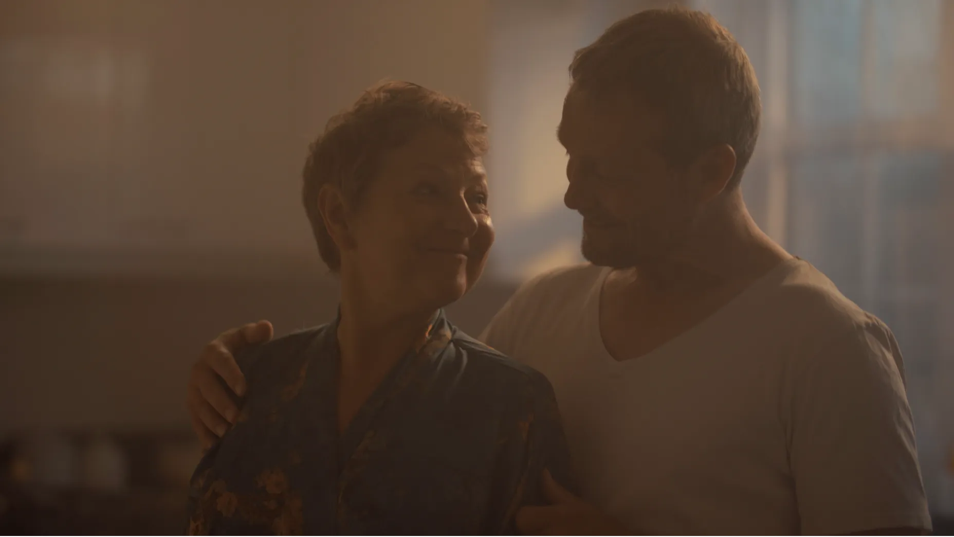 A man and woman smile at one another in a kitchen