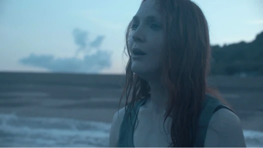 A woman with long hair standing in the sea, gazing towards the horizon.