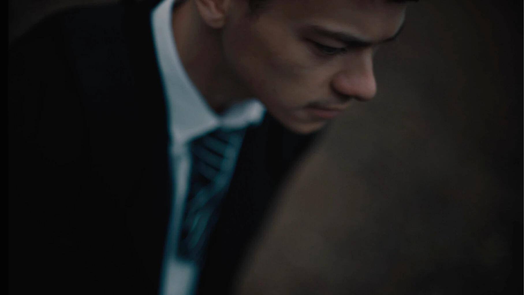 Close-up of young person in school uniform with striped tie looking downward in contemplative pose