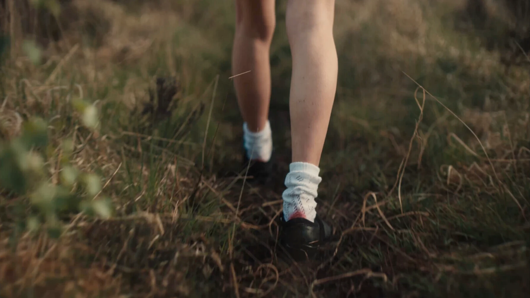 Person walking or running on natural grass trail wearing white athletic socks and black shoes