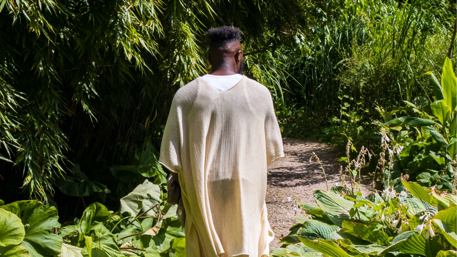 Dance Artist Chris Fonseca centre of the image walking along a path in a garden.