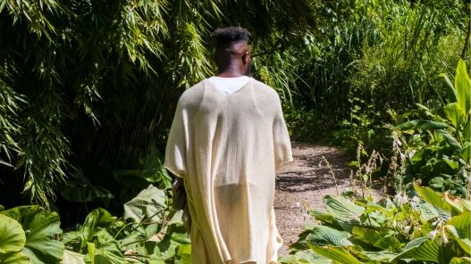 Dance Artist Chris Fonseca centre of the image walking along a path in a garden.