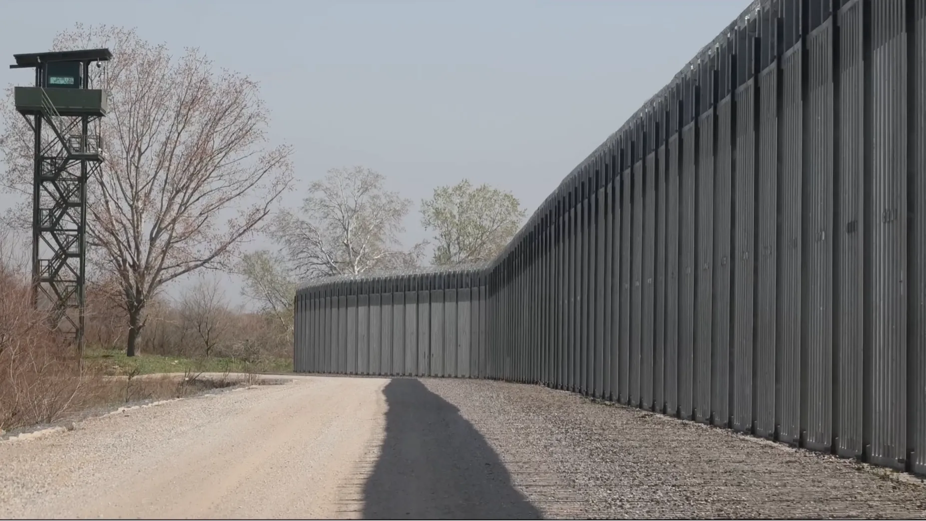 A high fence border wall with barbed wire and guard tower