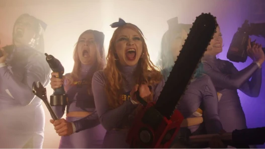 Five cheerleaders brandishing powertools in multi-coloured lighting, apparently screaming as if charging into battle