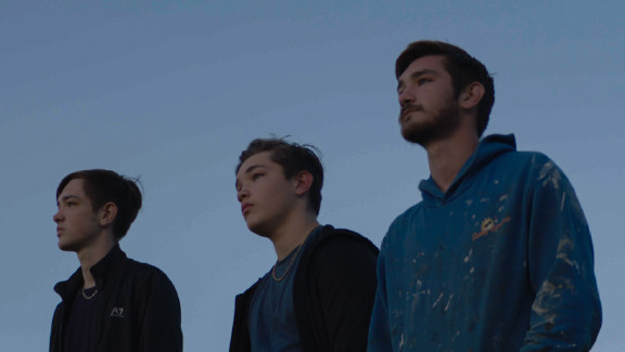 Three young men standing side by side looking out into the distance.